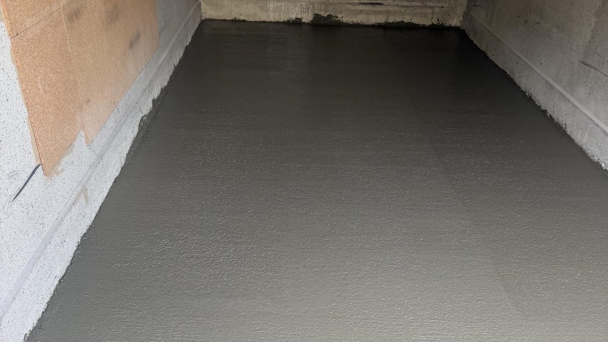 Raum mit frisch aufgetragener grauer Masse auf dem Boden, Wand mit Holzfaserplatten