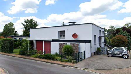 Modernes Flachdachhaus mit Einfahrt, Hecke und parkendem Kleinwagen an der Straße