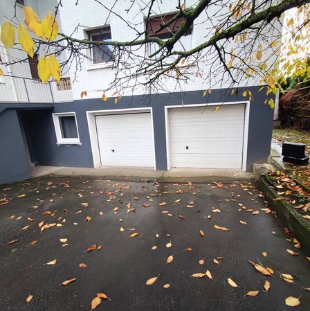 Nasse Einfahrt mit zwei Garagentoren und herabgefallenen Blättern