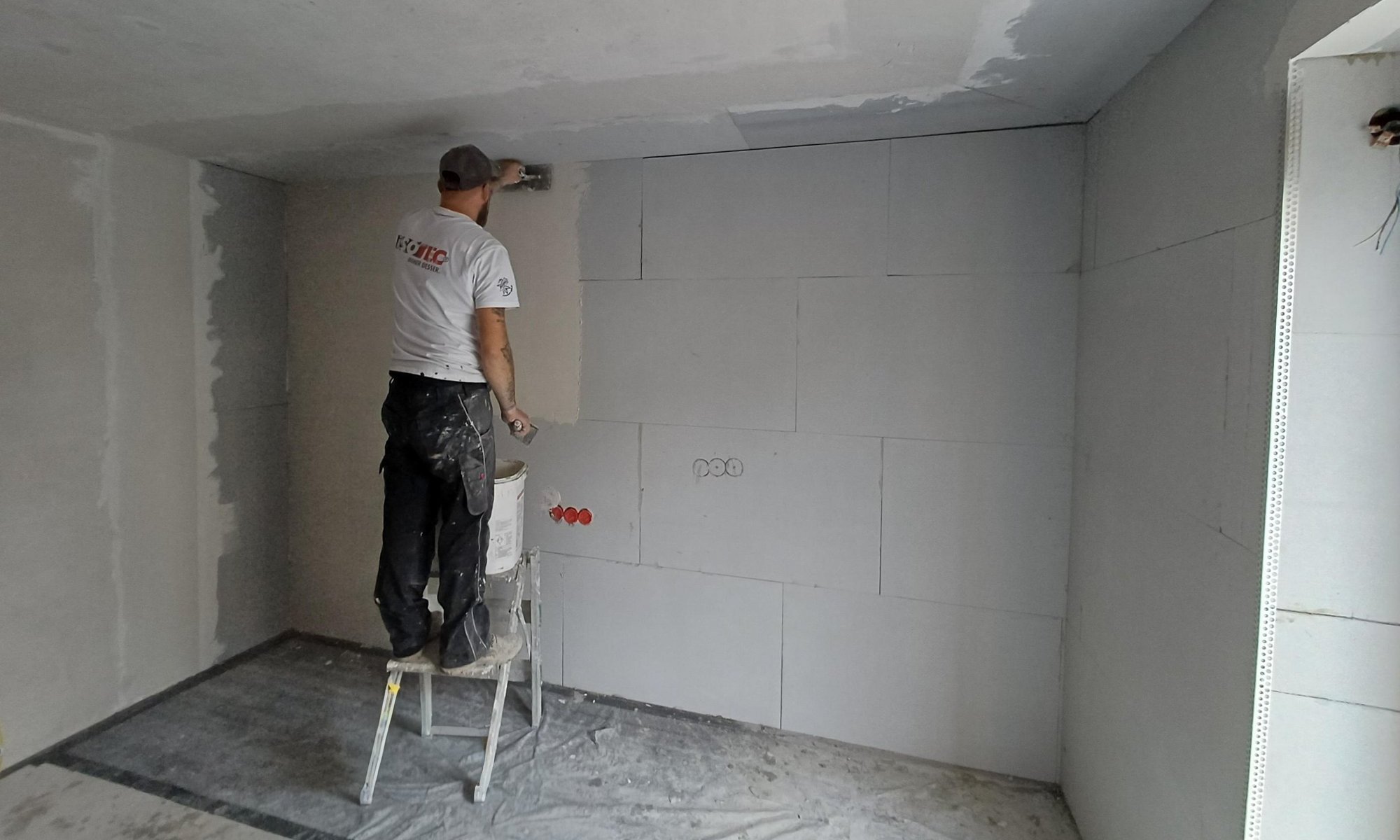 ISOTEC Mitarbeiter trägt graue Masse auf Zimmerwand auf.