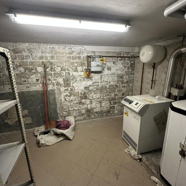 Kellerraum mit fleckiger Mauerwand, Heizgerät und freiliegenden Leitungen