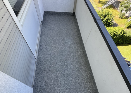 Schmaler Balkon mit grau gesprenkeltem Bodenbelag und heller Brüstung