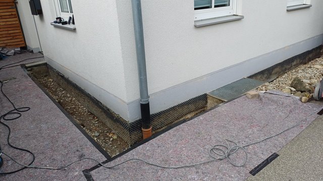 Freigelegte Kellerwand mit schwarzer Noppenbahn und Kiesstreifen am Gebäude