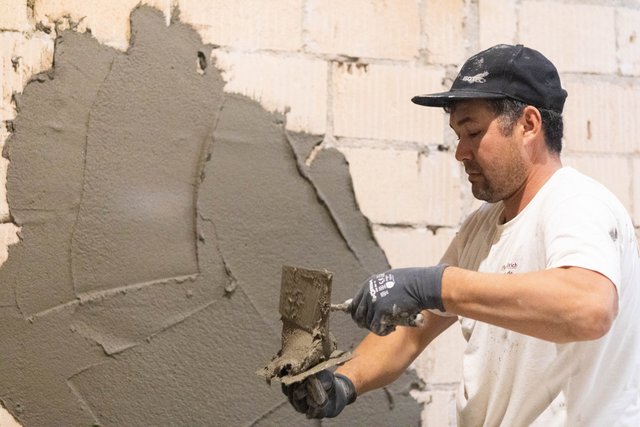 Arbeiter trägt graue Masse auf Kellerwand auf.