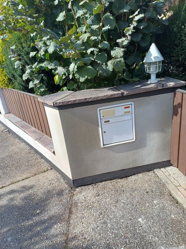 Grundstücksmauer mit Briefkasten, Leuchte und Steinabdeckung am Gehweg