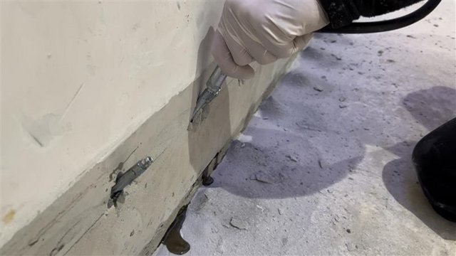 Hand mit Injektionsgerät an Kellerwand, graue Masse tritt aus Bohrlöchern aus