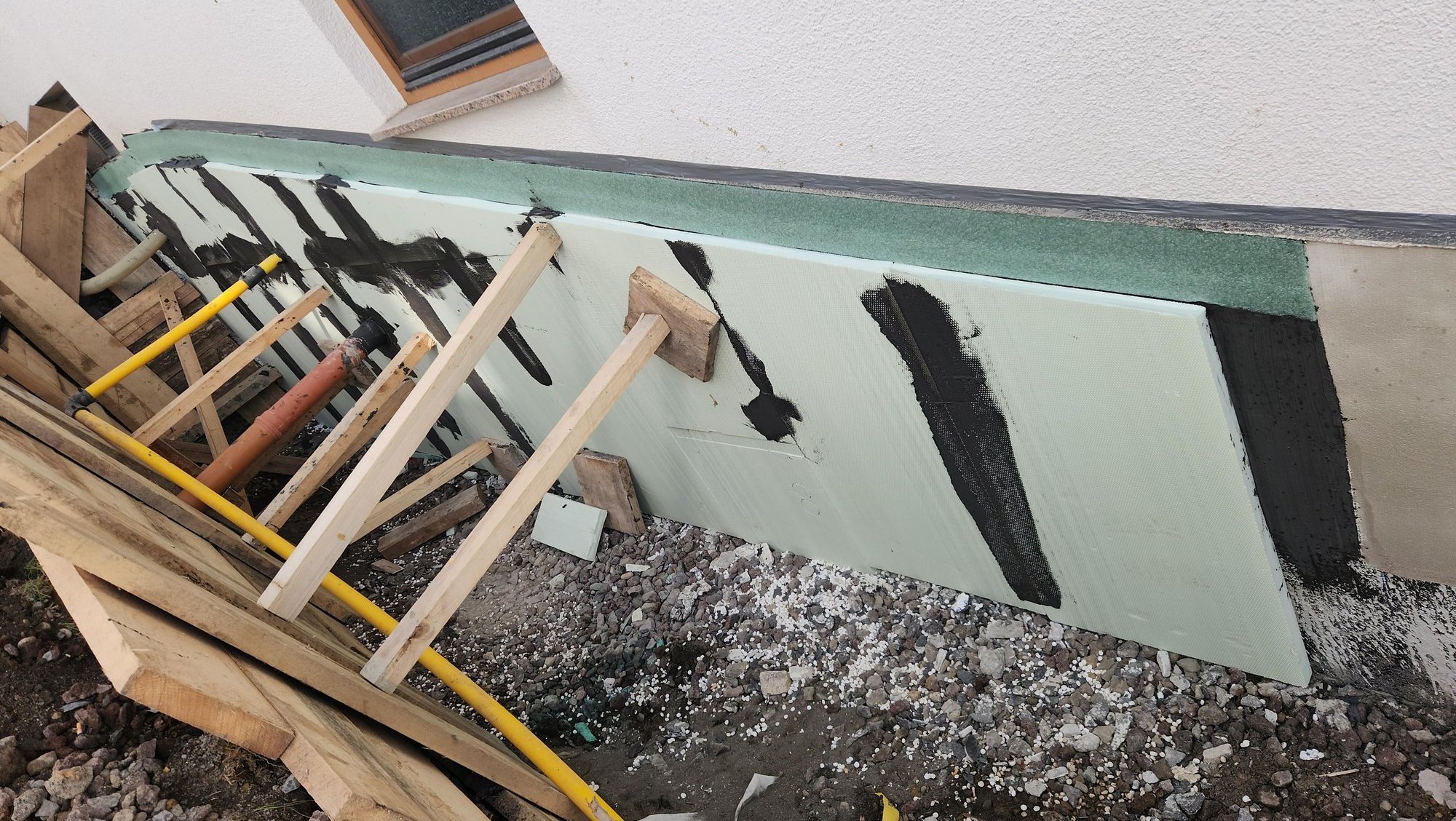 Dämmplatten mit schwarzen Klebestreifen an Sockelzone, Holzgestell und Rohboden davor