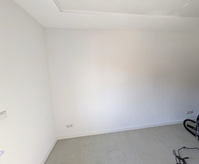 Leerer Raum mit weißer Wand, Steckdosen und grauem Fliesenboden.