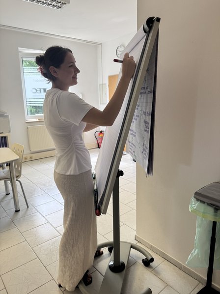 Person schreibt mit rotem Stift auf Flipchart im hellen Seminarraum.
