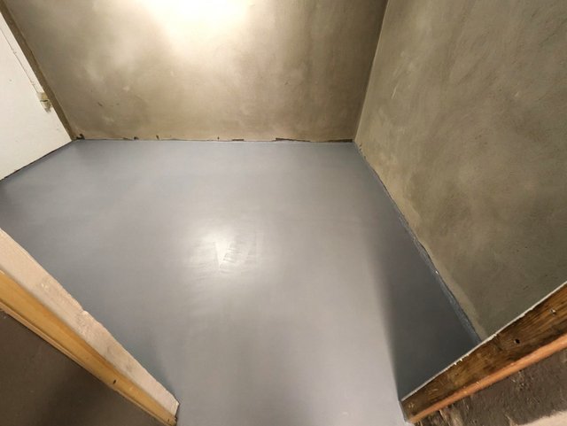 Glatter grauer Bodenbelag in kleinem Raum, Betonwände und Türrahmen sichtbar