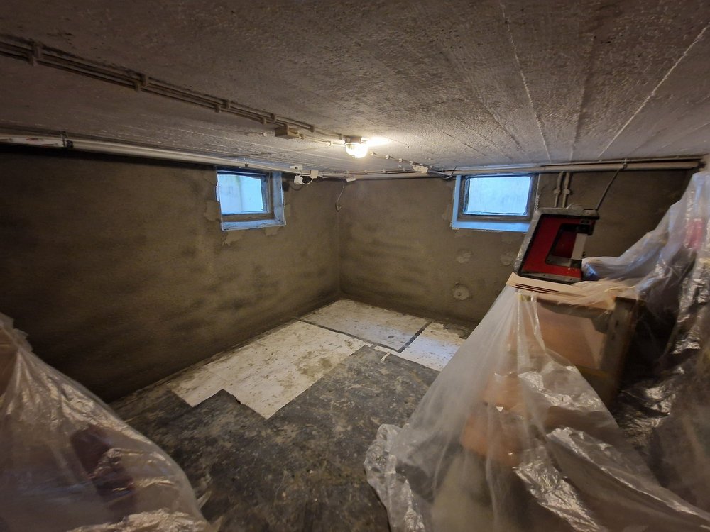 Kellerraum mit abgedichteten Wänden, kleinen Fenstern und abgedeckten Möbeln