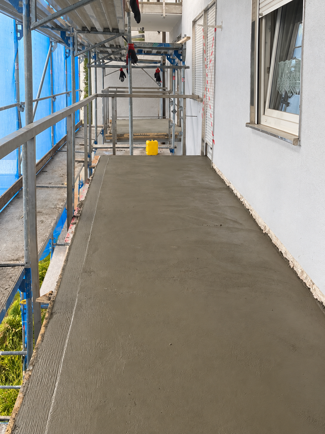 Frischer grauer Estrich auf Balkonboden, Baugerüst neben weißer Fassade