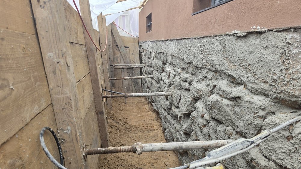 Freigelegte Gebäudewand im schmalen Erdgraben mit Holzverbau und Stahlstützen