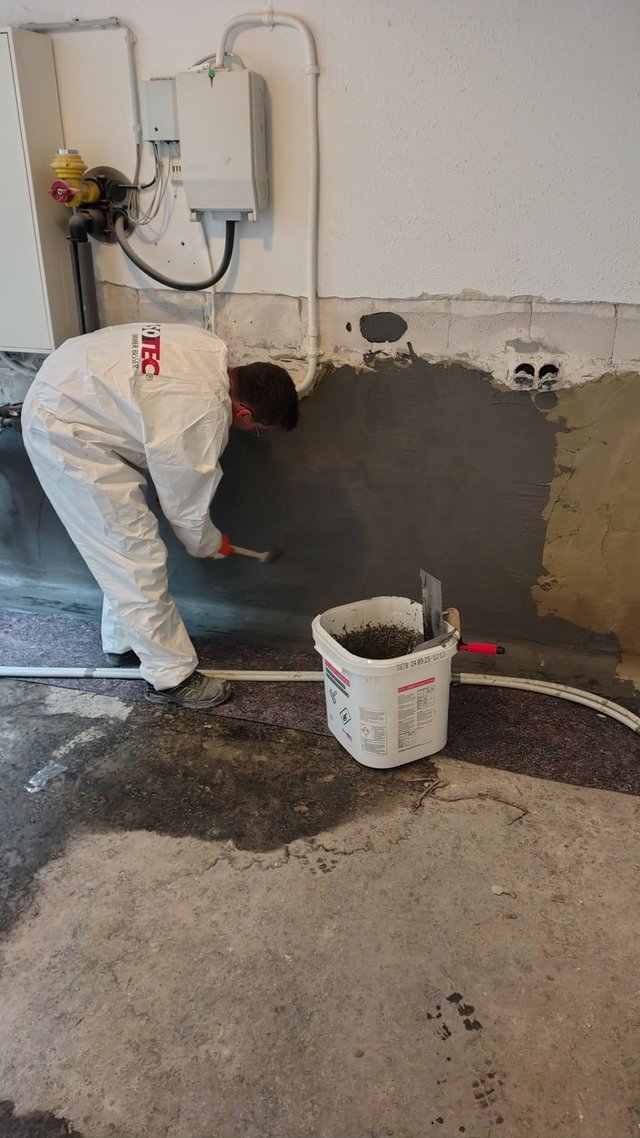 ISOTEC Mitarbeiter trägt graue Masse auf Kellerwand auf