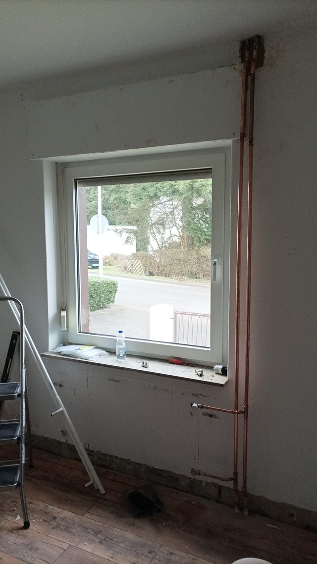 Freigelegte Kupferrohre verlaufen neben Fenster in renoviertem Zimmer.
