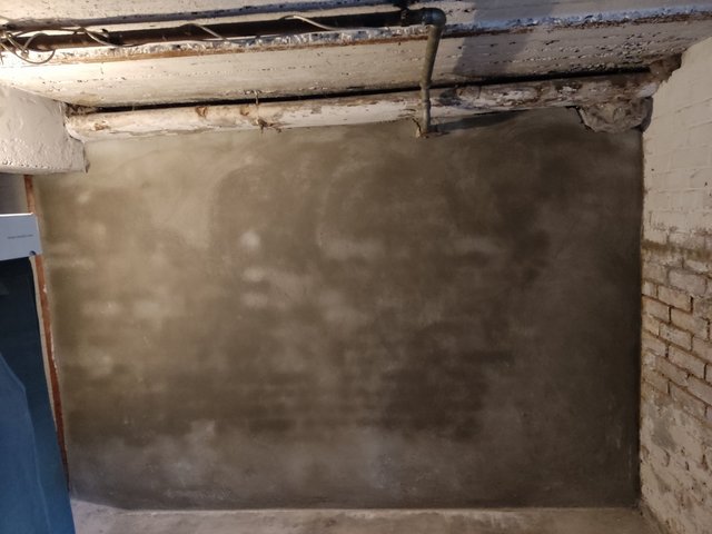 Graue Masse auf Kellerwand, freiliegende Rohre unter Betondecke