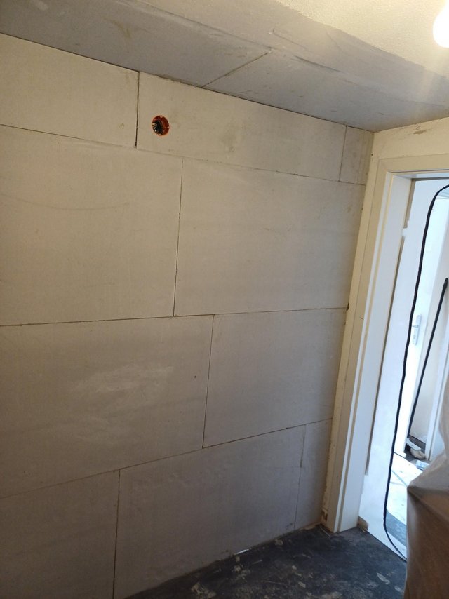 Wand mit hellen Platten und sichtbaren Fugen neben Türöffnung