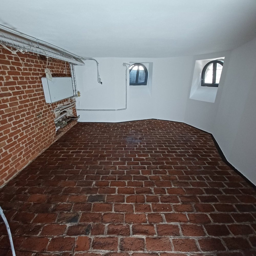 Gewölberaum mit Ziegelboden, Backsteinwand und zwei Rundbogenfenstern