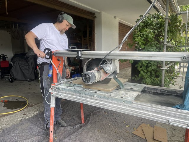Arbeiter schneidet helle Platte mit elektrischer Steinsaege auf Baustelle.