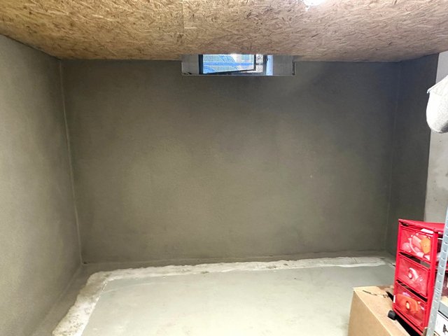 Graue beschichtete Kellerwand mit kleinem Fenster und rotem Werkzeugkoffer im Vordergrund