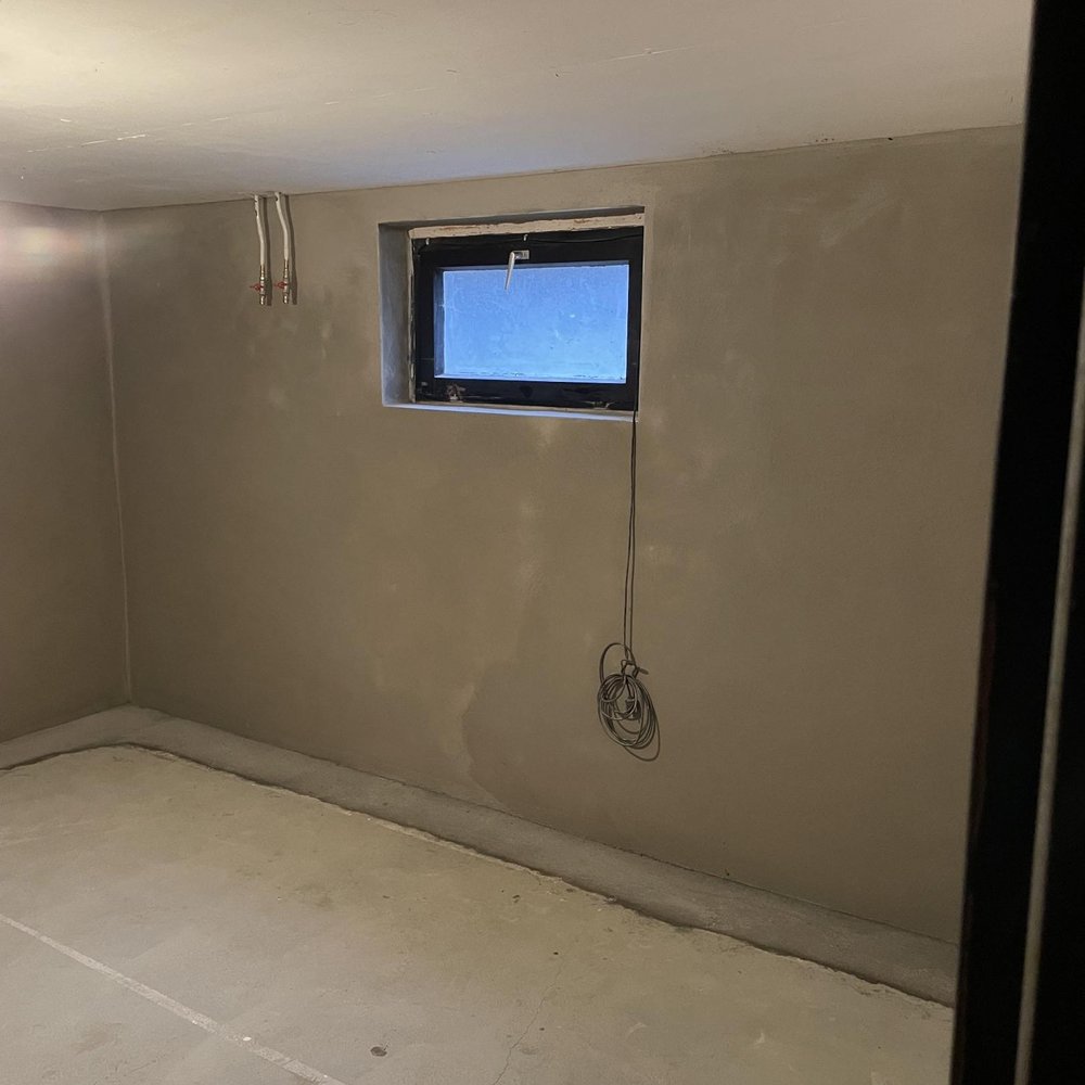 Kellerraum mit grauer Wandbeschichtung, kleinem Fenster und freiliegenden Leitungen