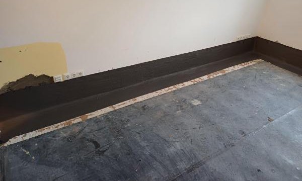 Schwarze Masse am Wand-Boden-Anschluss in Raum, freigelegter Estrichstreifen