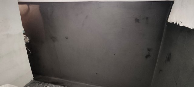 Dunkle Wandfläche mit schwarzen Flecken und unregelmäßigen Spuren in einem Innenraum.