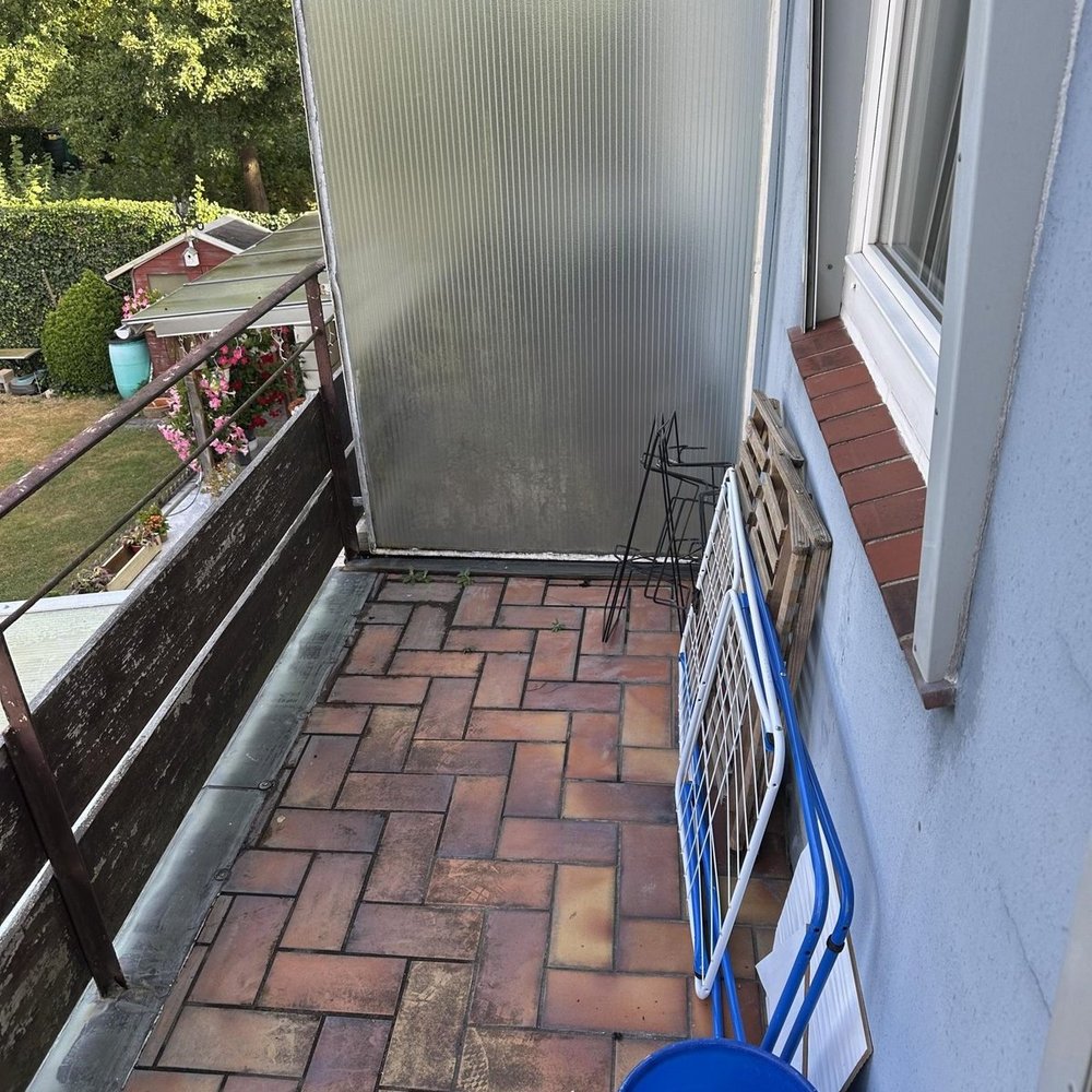 Schmaler Balkon mit Fliesenboden, Sichtschutzplatte und abgestellten Gestellen am Fenster