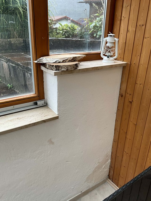 Fensterbank mit weißer Laterne und Holzscheiben auf heller Steinplatte