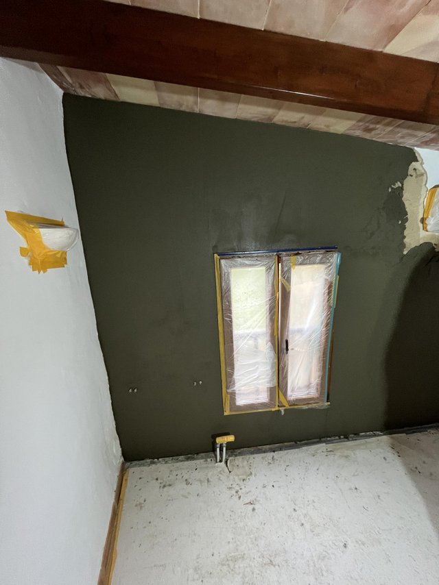 Abgeklebtes Fenster, dunkelgraue Masse auf Wand, sichtbare Holzbalken im Raum.