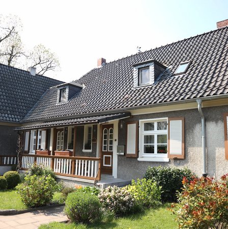 Einfamilienhaus mit dunklem Ziegeldach, Gaubenfenstern, Fensterläden und Vorgarten.