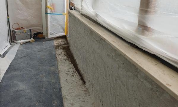 Abgeklebter Arbeitsbereich mit Folienwänden, grauer Masse auf Betonbrüstung und Schutzvlies am Boden
