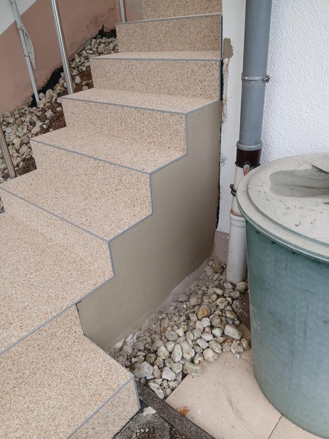 Geflieste Außentreppe neben Fallrohr und Kiesbett