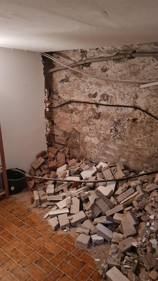 Freigelegte Kellerwand mit Kabeln, davor Schutt aus Mauersteinen auf Fliesenboden