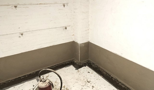 Schwarze Abdichtung im unteren Bereich einer Kellerwand, Raumecke