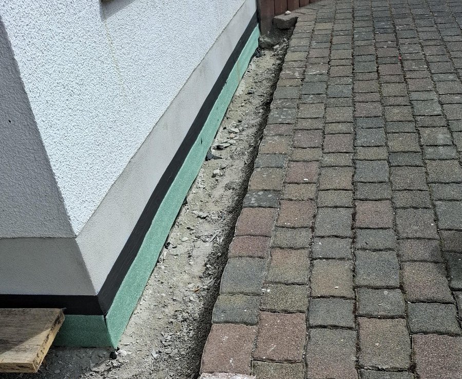 Aufgenommene Pflastersteine neben Hausfassade, Randstreifen ausgehoben, Steine liegen lose.