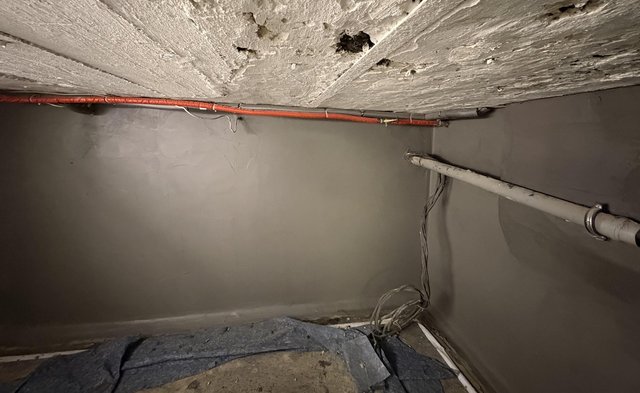 Abplatzende Betondecke mit Löchern und Leitungen in kleinem Kellerraum