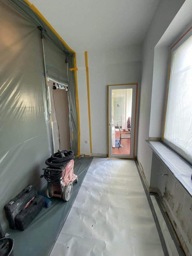 Abgeklebter Raum mit Trocknungsgerät und beschädigtem Wandbereich unter dem Fenster
