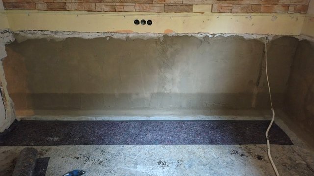 Frisch geglättete graue Masse auf Kellerwand über Sockelbereich, Steckdosenöffnung sichtbar
