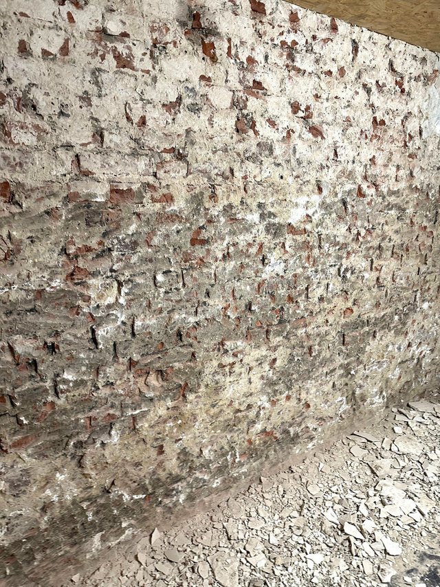 Freigelegte Ziegelwand mit abgeplatzter heller Schicht, Bruchstücke am Boden.