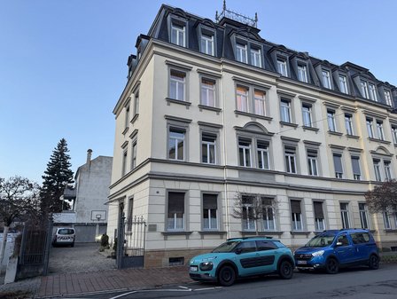 Mehrstöckiges Altbauwohnhaus an Straße mit parkenden Autos