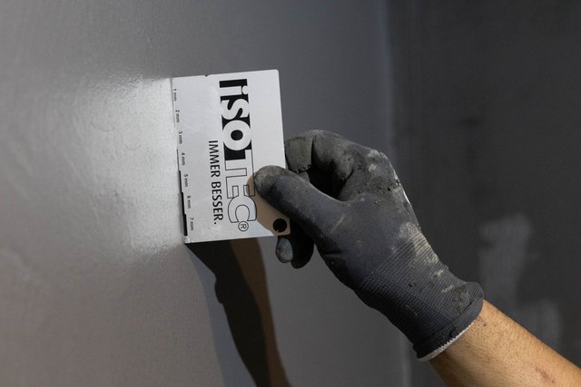 ISOTEC Mitarbeiter misst Schichtdicke an grauer Wand mit Messkarte
