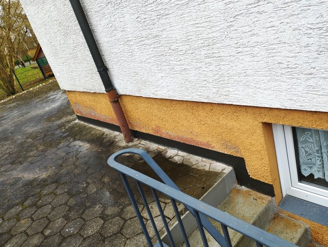 Verfärbte Außenfassade mit Regenfallrohr und kleinem Treppenabgang