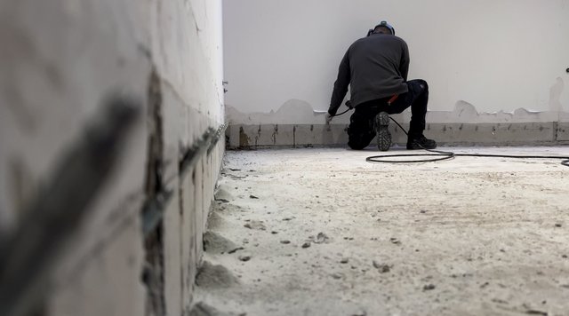 Arbeiter injiziert Material in Bohrlöcher entlang der Wand am Boden.