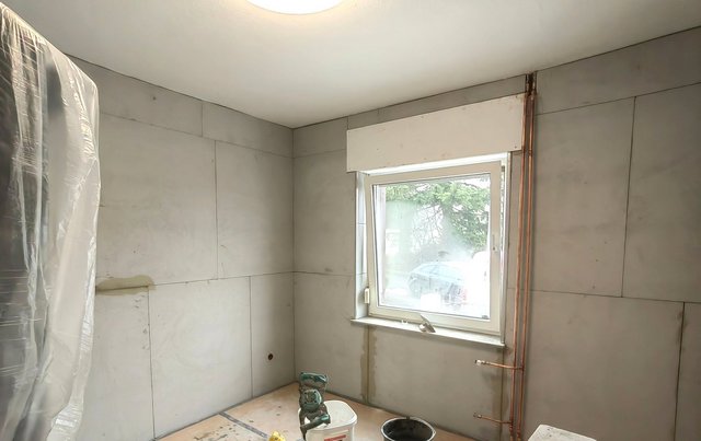 Helle Platten an Zimmerwänden, Fenster und freiliegende Kupferrohre im renovierten Raum