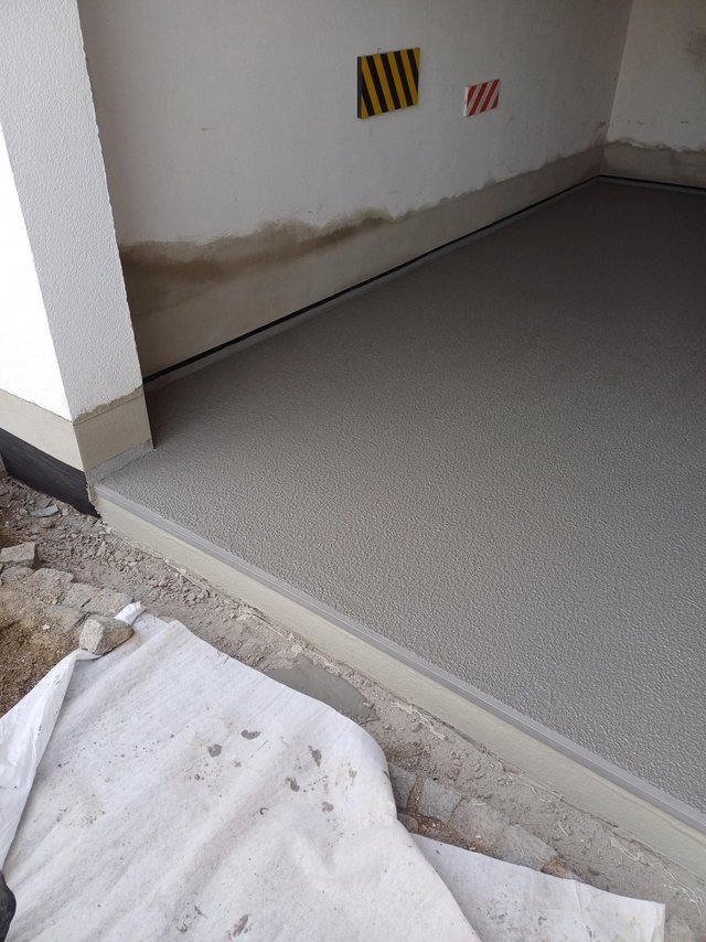 Feuchter Sockelbereich an Wand neben beschichtetem Boden, Nahaufnahme