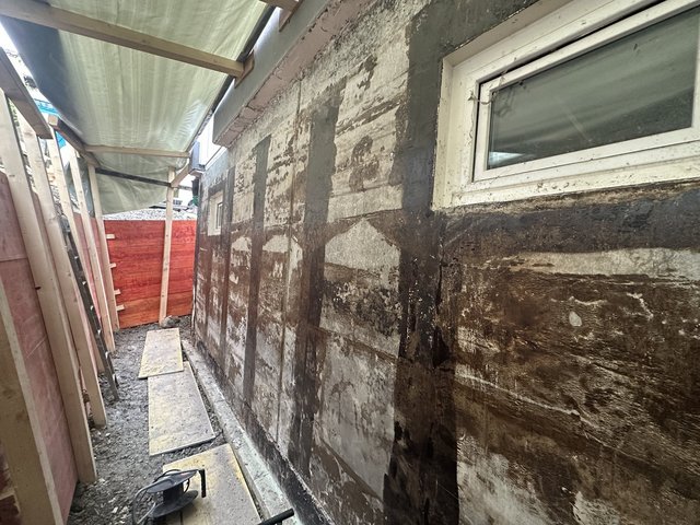 Schwarze Masse auf Kellerwand mit Fenstern, Außenaufnahme im Gerüstgang