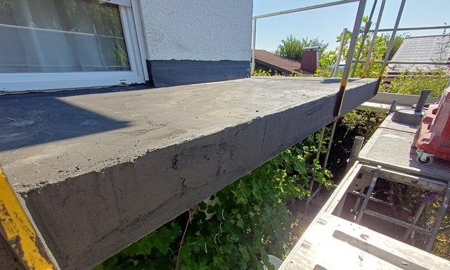 Frisch geglättete Beton-Balkonplatte mit schwarzer Masse am Sockel, Gerüst daneben