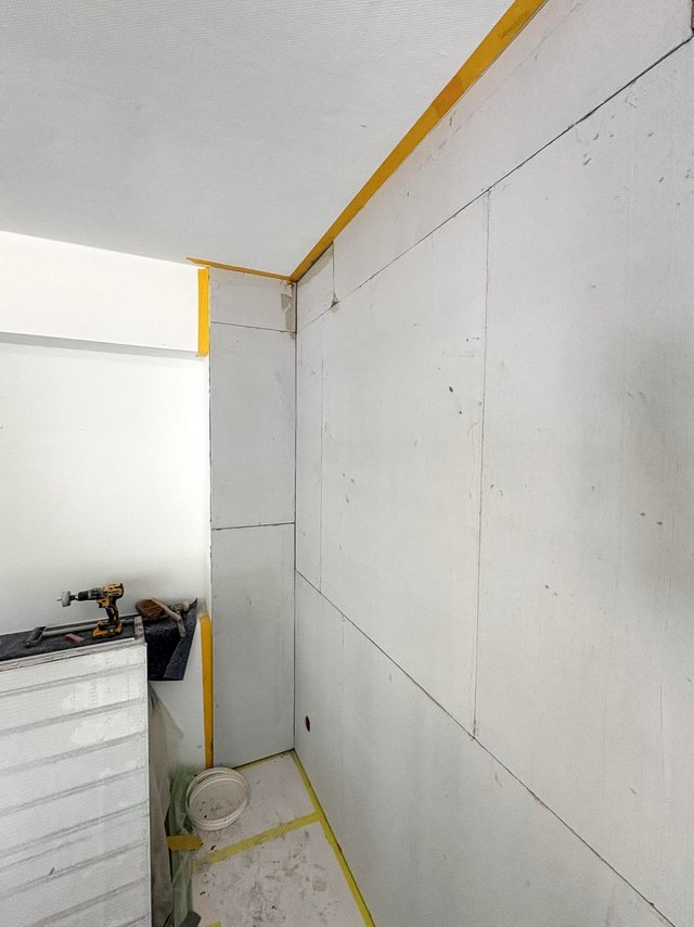 Renovierungsbereich mit hellen Wandplatten und gelbem Abklebeband, Bohrschrauber auf Abdeckung