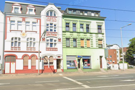 Zwei bunte Altbaufassaden an Straßenkreuzung, Schaufenster im Erdgeschoss, blauer Himmel